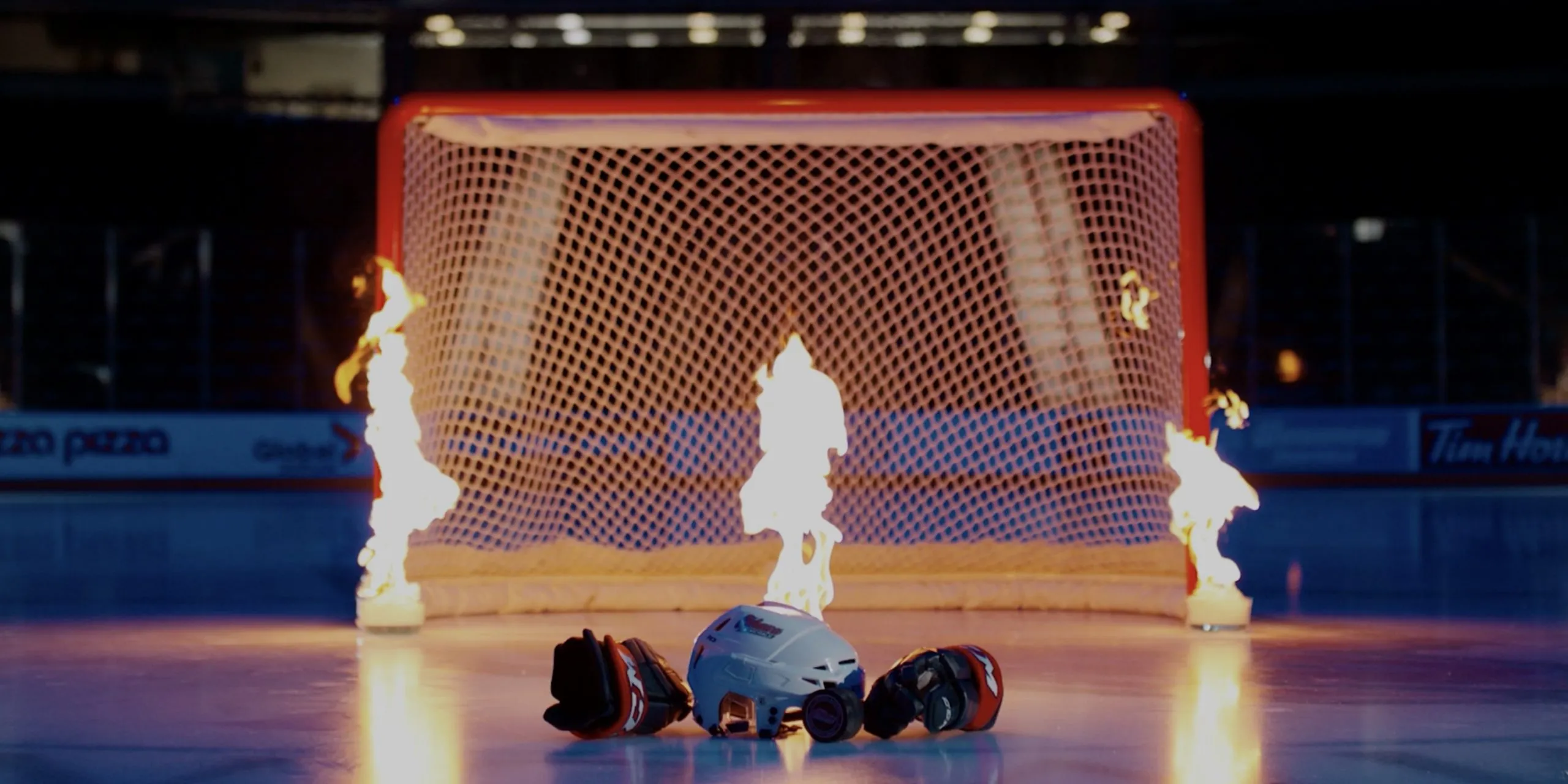 a hockey helmet on fire in between glove in front of a hockey net on fire on a ice rink